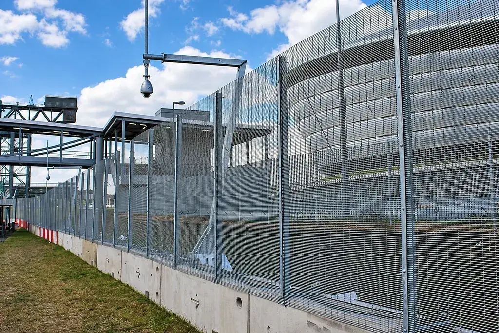 Surveillance camera mounted beside a mesh security fence