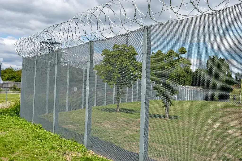 View across grass and trees through a security mesh fence