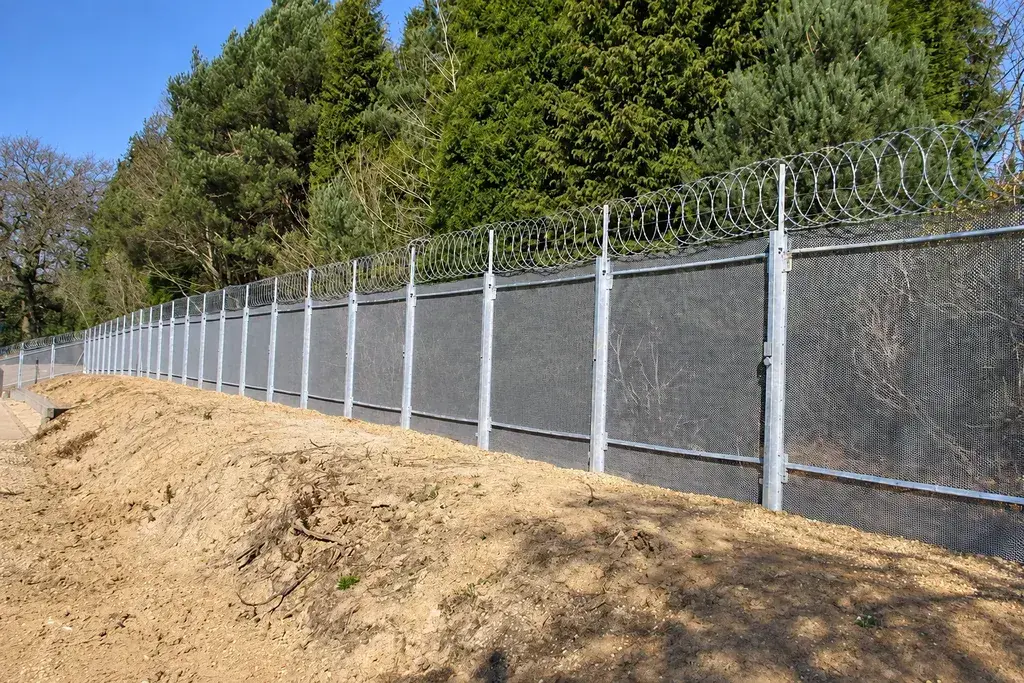 Fine mesh perimeter fence with security topping beside trees