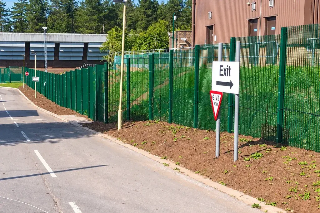 Green security mesh fence and posts along a site road