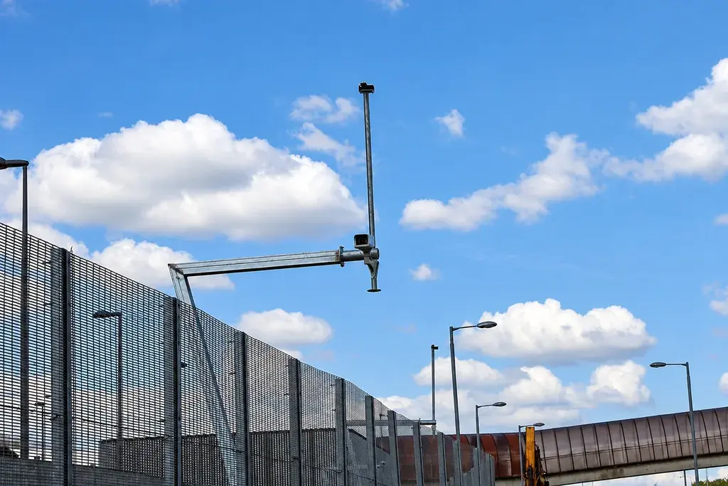 Surveillance camera positioned above a security mesh fence