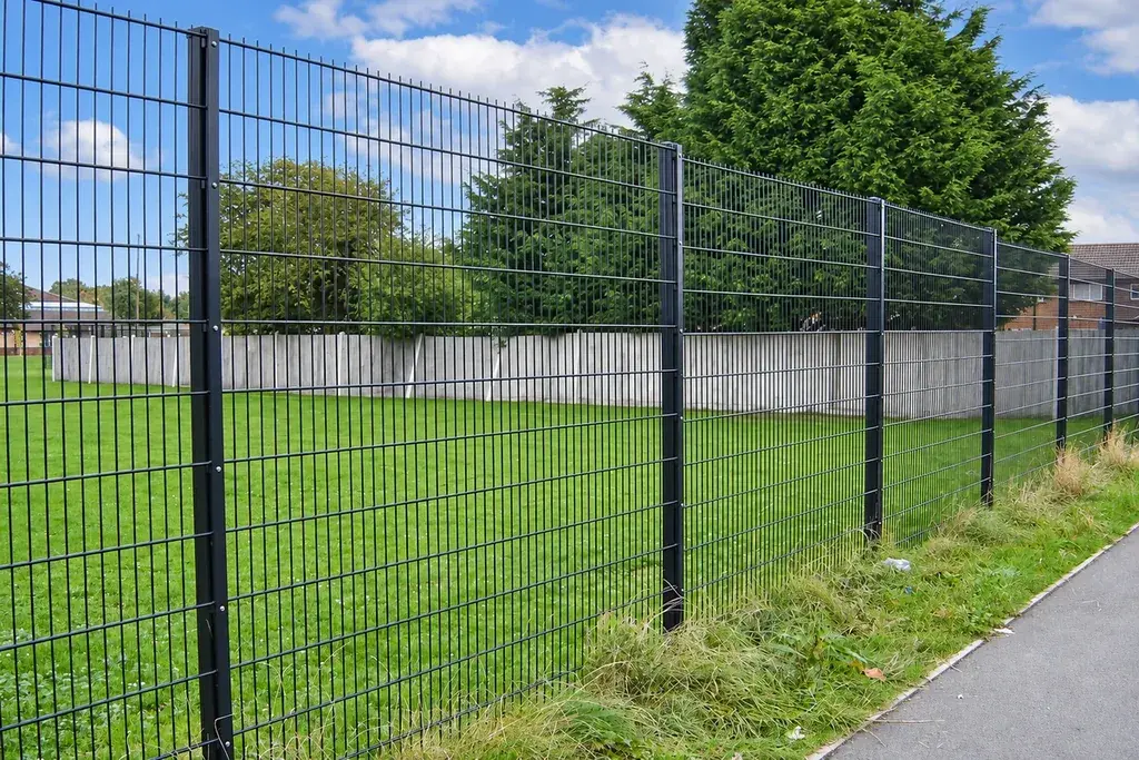 Dark double wire fence around a grass sports field