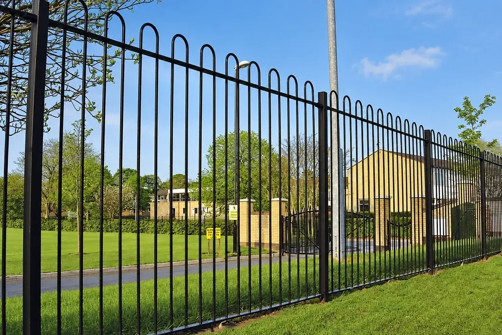 Black bow-top railing with curved crowns along a landscaped boundary