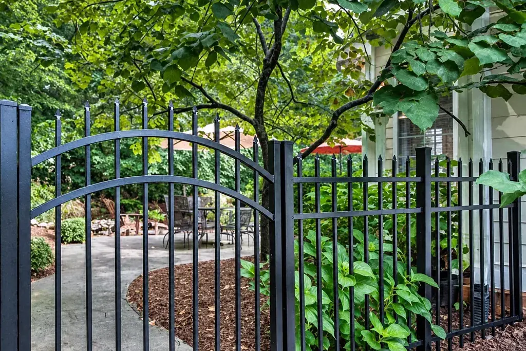 Black ornamental metal gate with curved top between matching fence panels