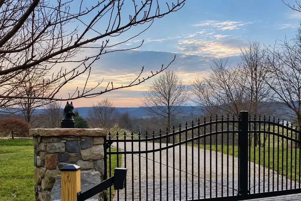 Black arched metal driveway gate between stone pillars