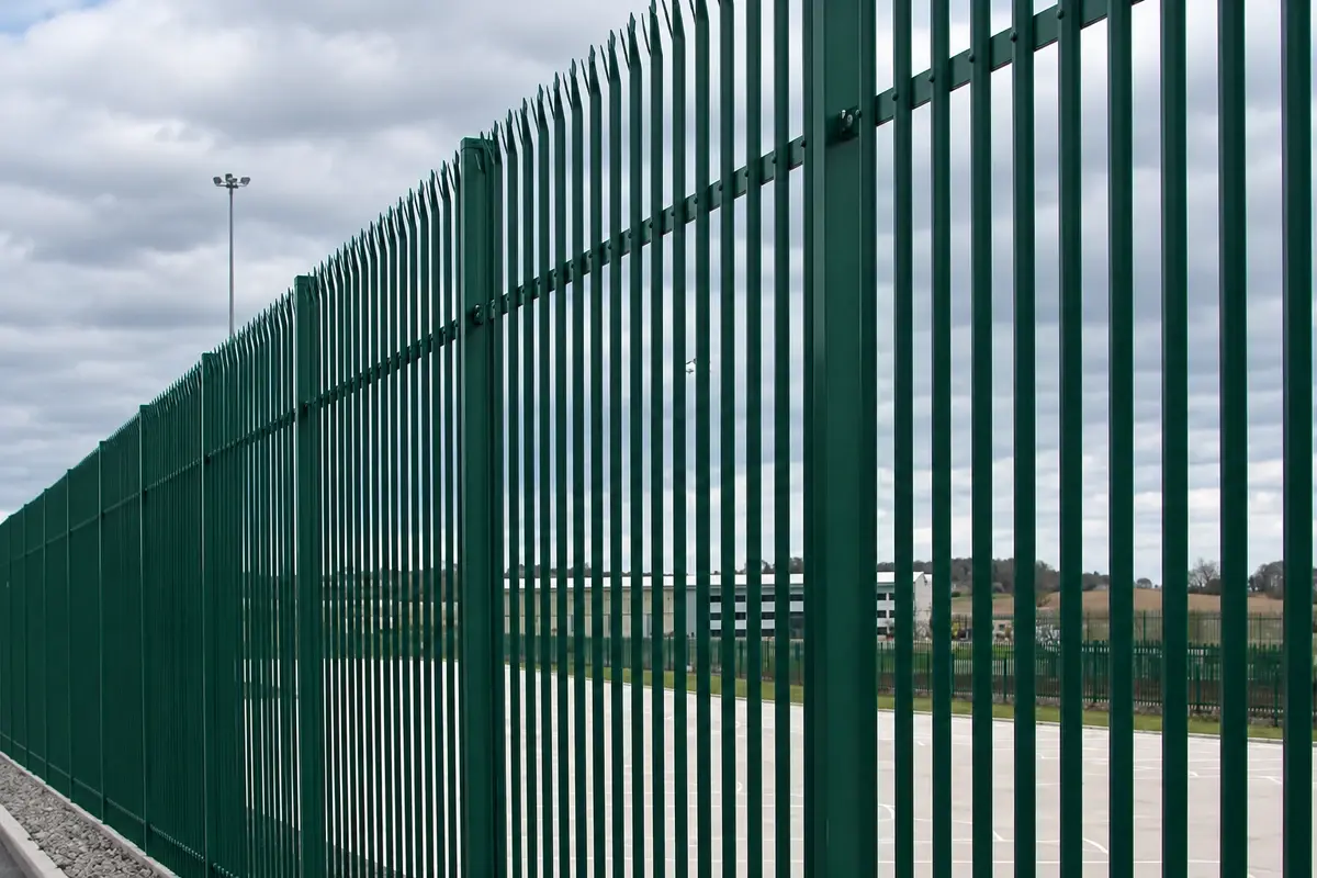Green palisade fence with repeated pales, rails and posts along a perimeter