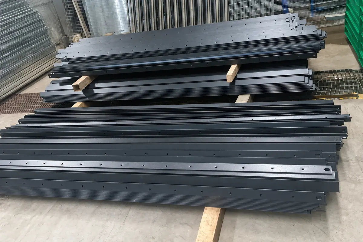 Stacks of black steel palisade fence rails with predrilled holes