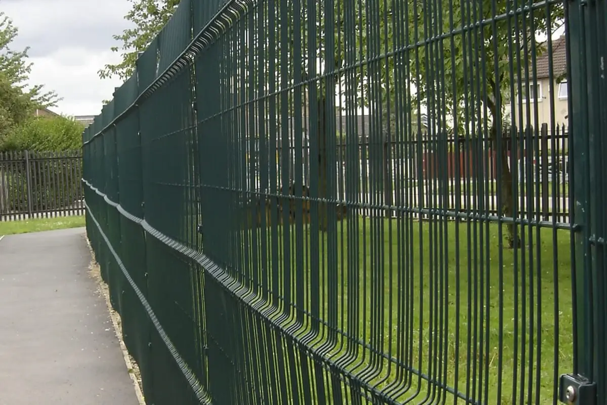 Green open welded mesh fence with the landscape visible through its grid