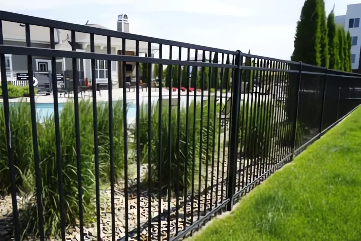 Black flat-top metal fence following a sloping landscaped boundary