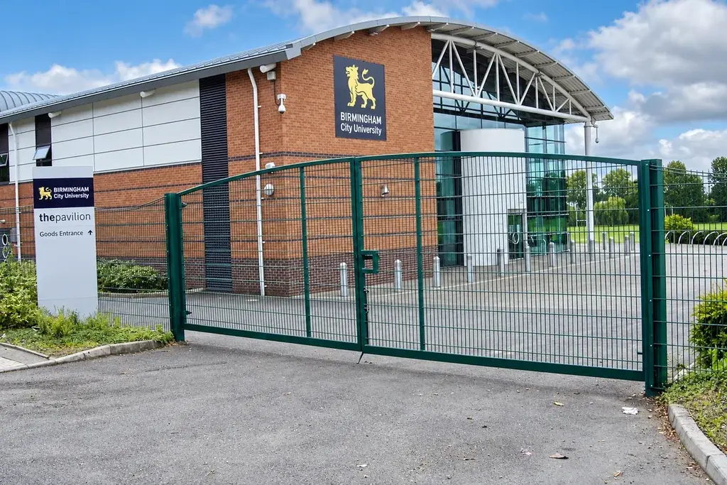 Green double-leaf mesh vehicle gate at a paved site entrance