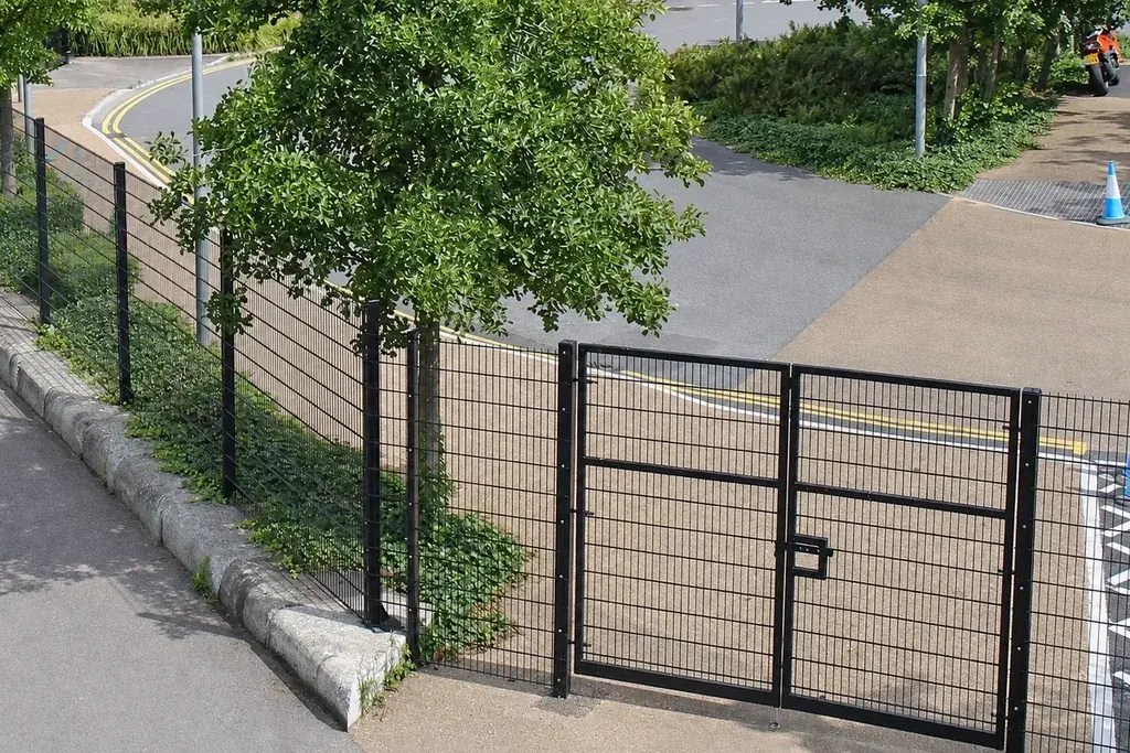 Double-leaf mesh gate viewed with adjoining fence and paved passage
