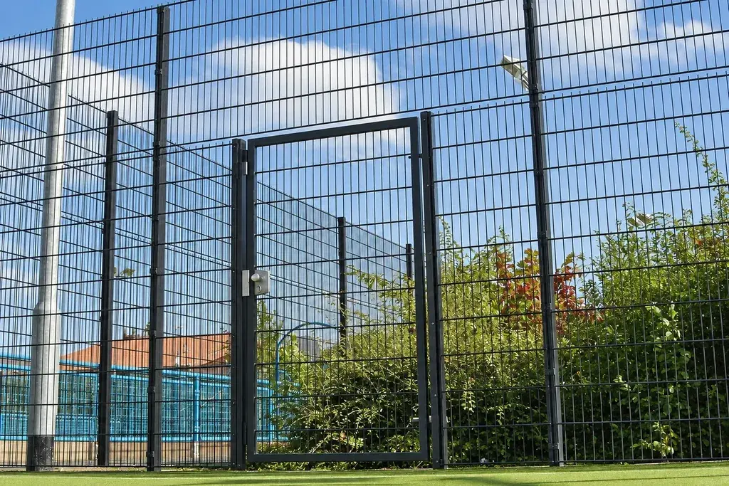 Single-leaf black mesh pedestrian gate set in a fence line