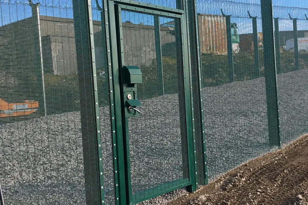 Green close-mesh pedestrian gate set within a security fence