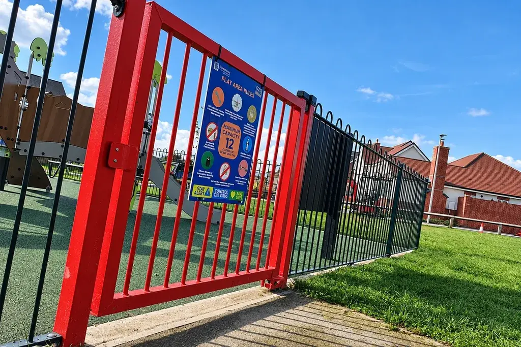 Red pedestrian gate at a fenced playground entrance