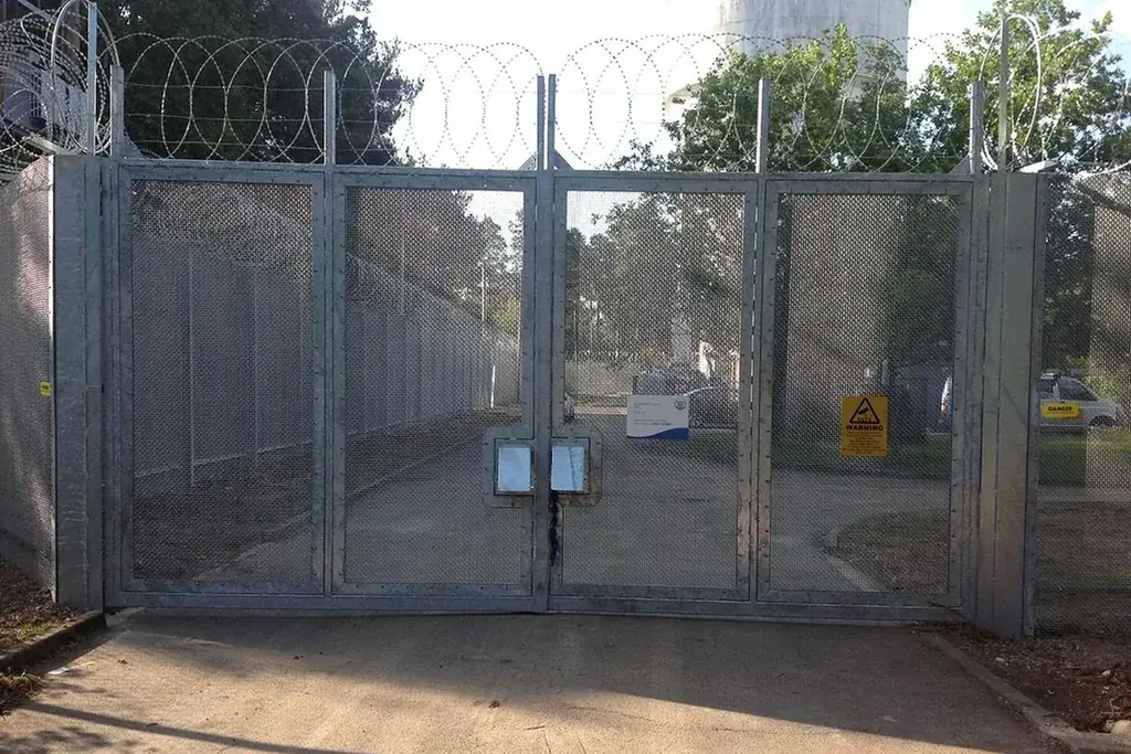 Double-leaf mesh vehicle gate with central closure and paved threshold