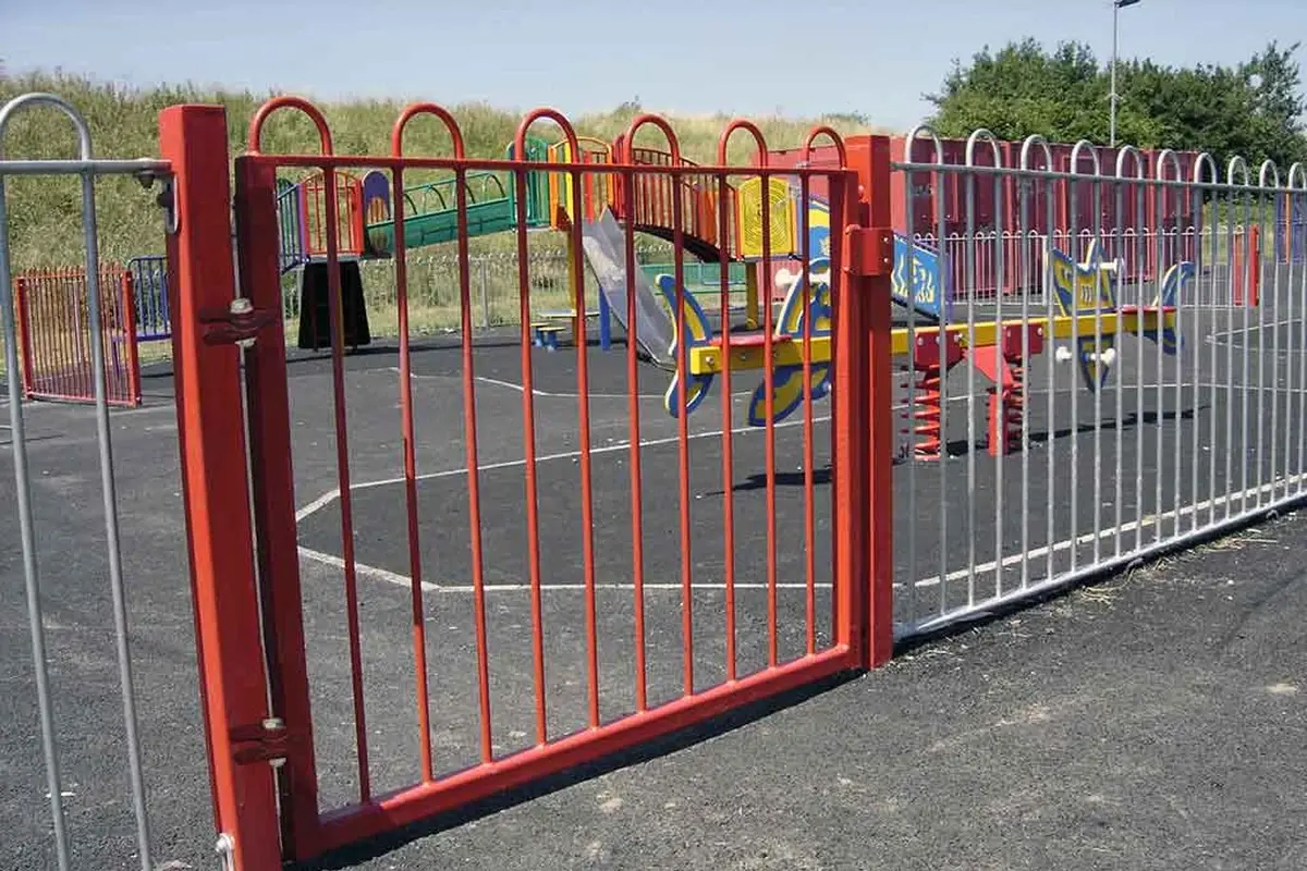 Red pedestrian gate and its supporting posts in a metal fence line