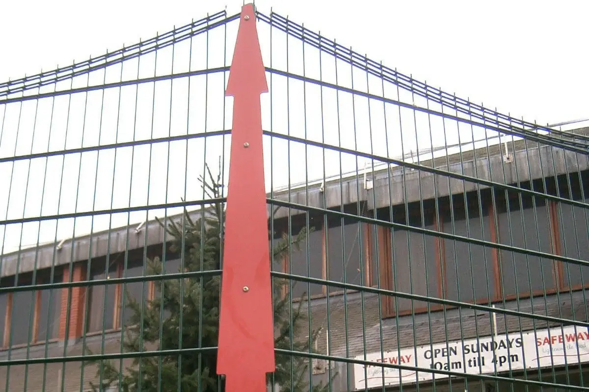 Red vertical clamp bar securing a mesh fence panel beside a post