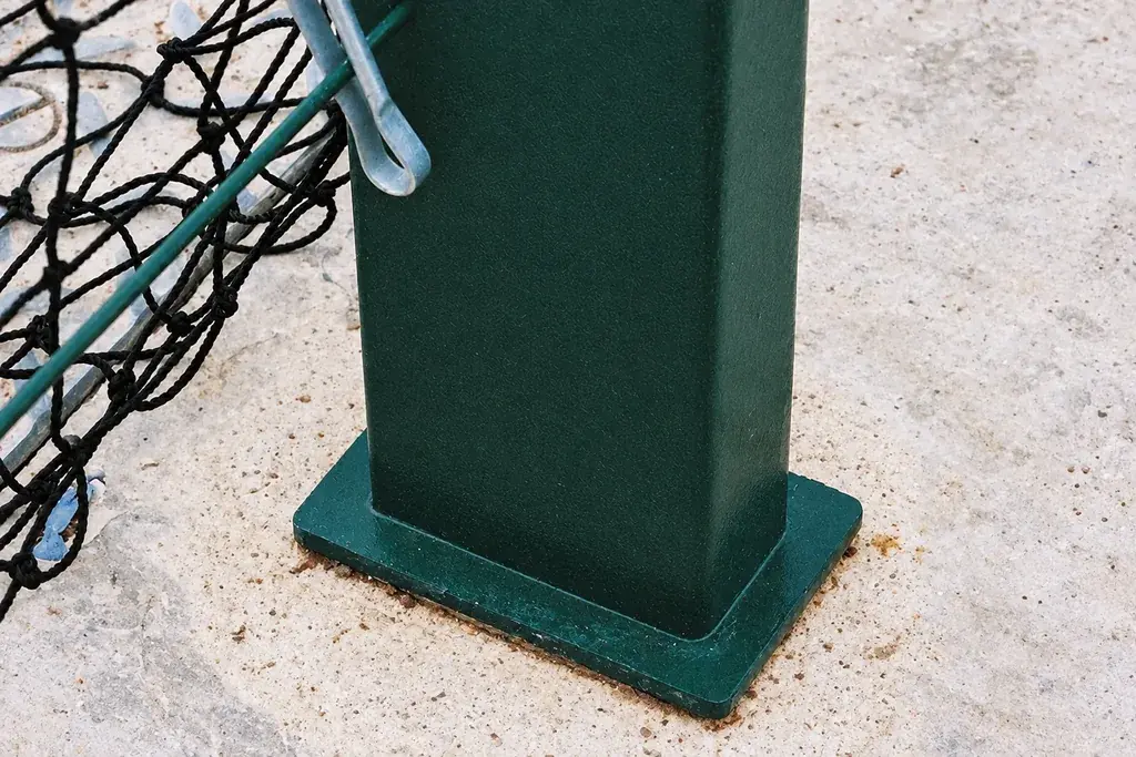 Green metal fence post on a base plate at a concrete surface