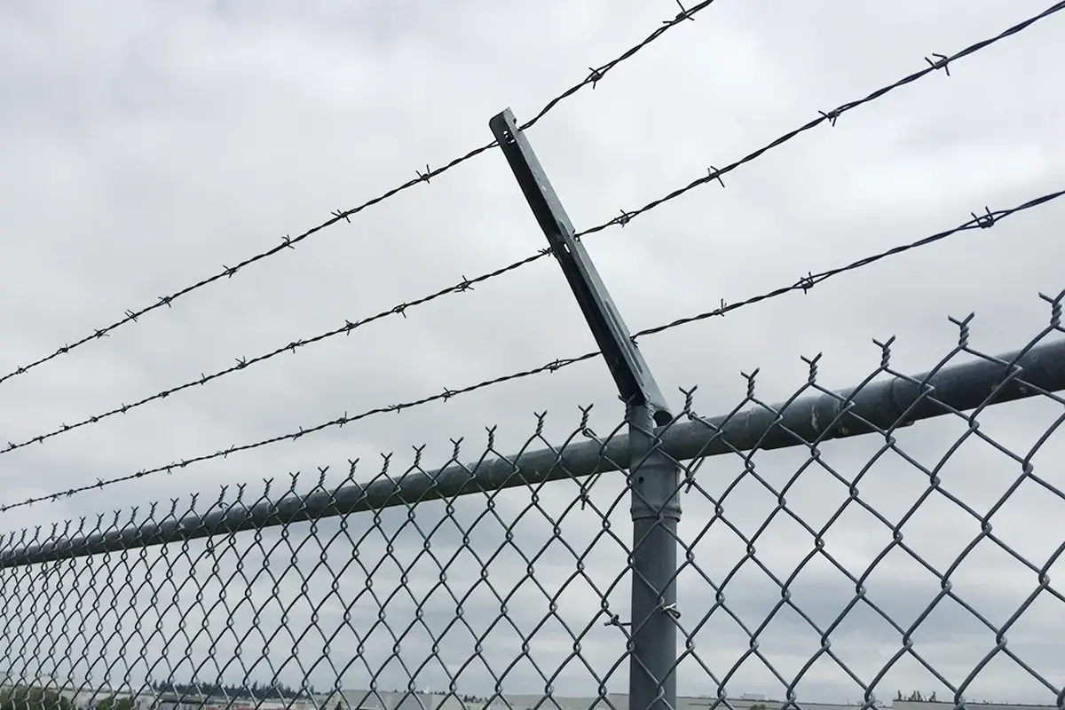 Angled metal fence extension arms carrying barbed wire above chain link mesh