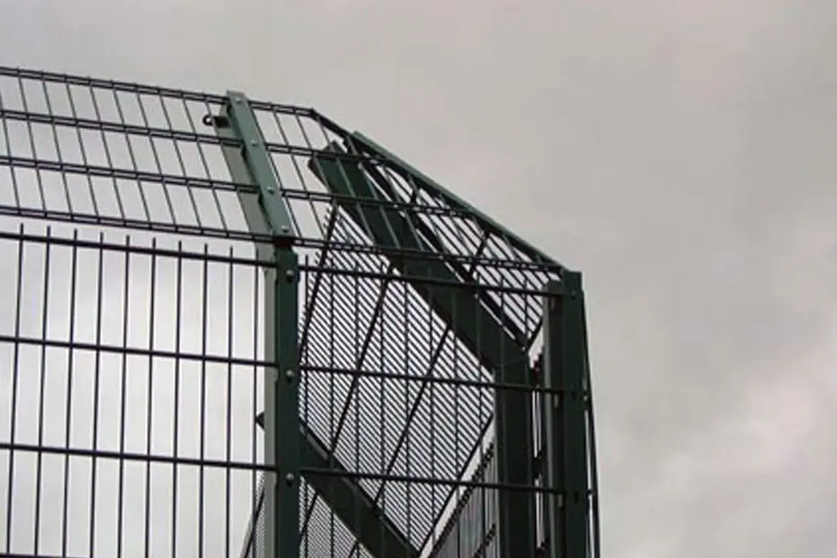 Cranked metal mesh topping above a green fence and gate position