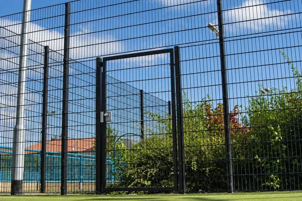 Pedestrian gate in a tall mesh sports enclosure