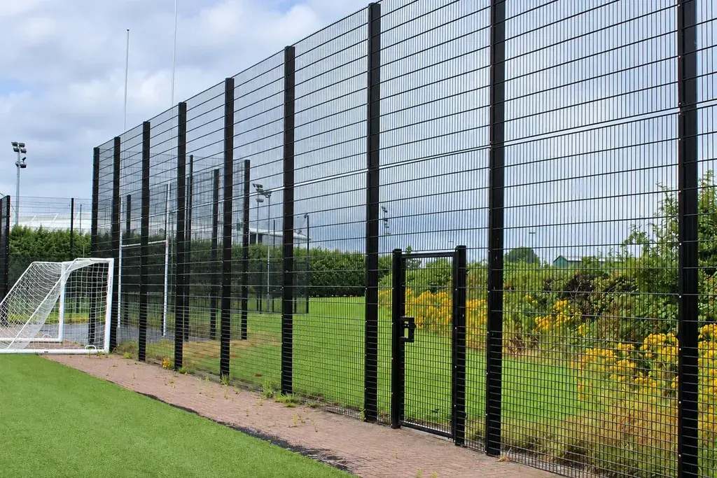 Tall mesh fencing along the side of a grass football pitch