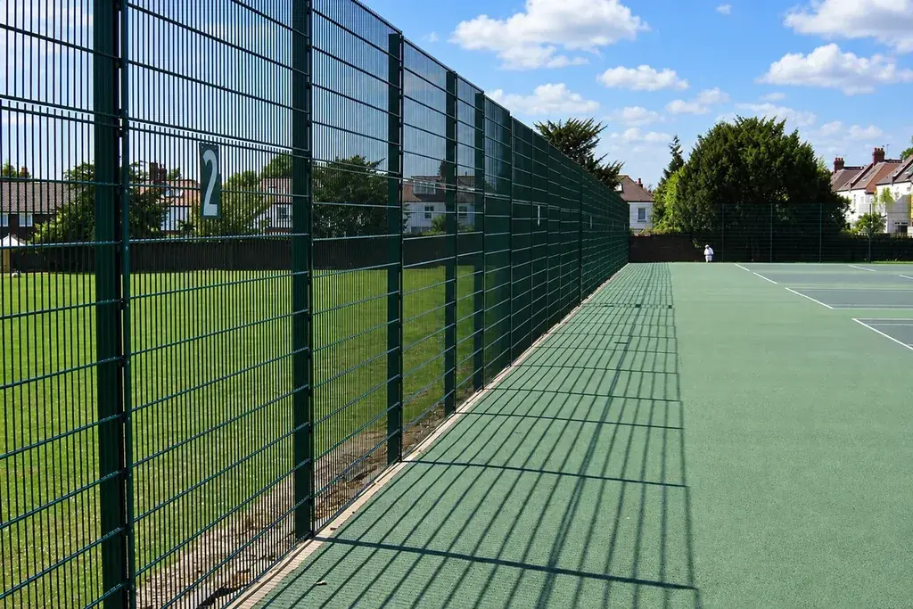 Tennis court side run beside a tall mesh perimeter fence