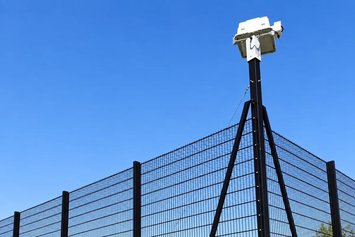 Floodlight mast beside a tall mesh sports fence