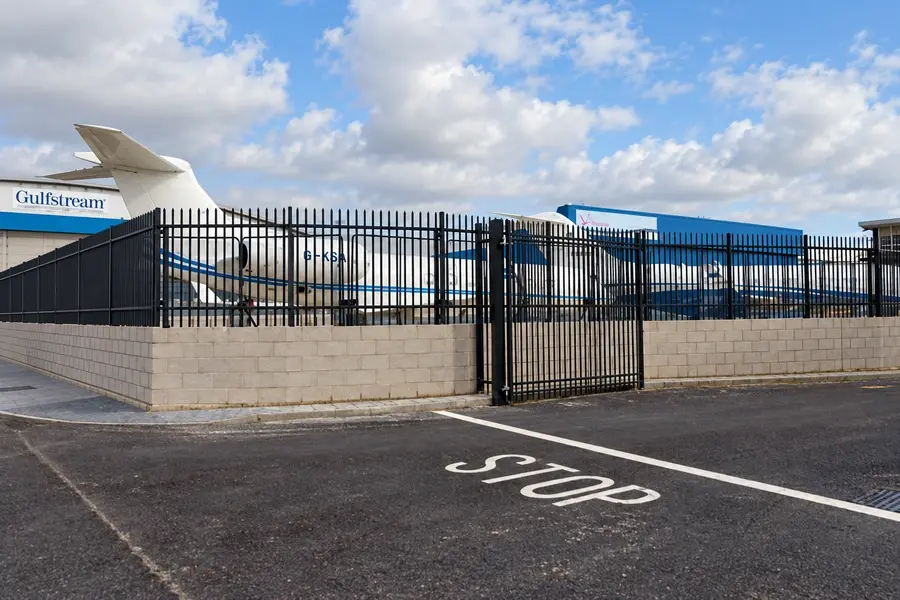 Black steel perimeter fence and gates beside an airport building