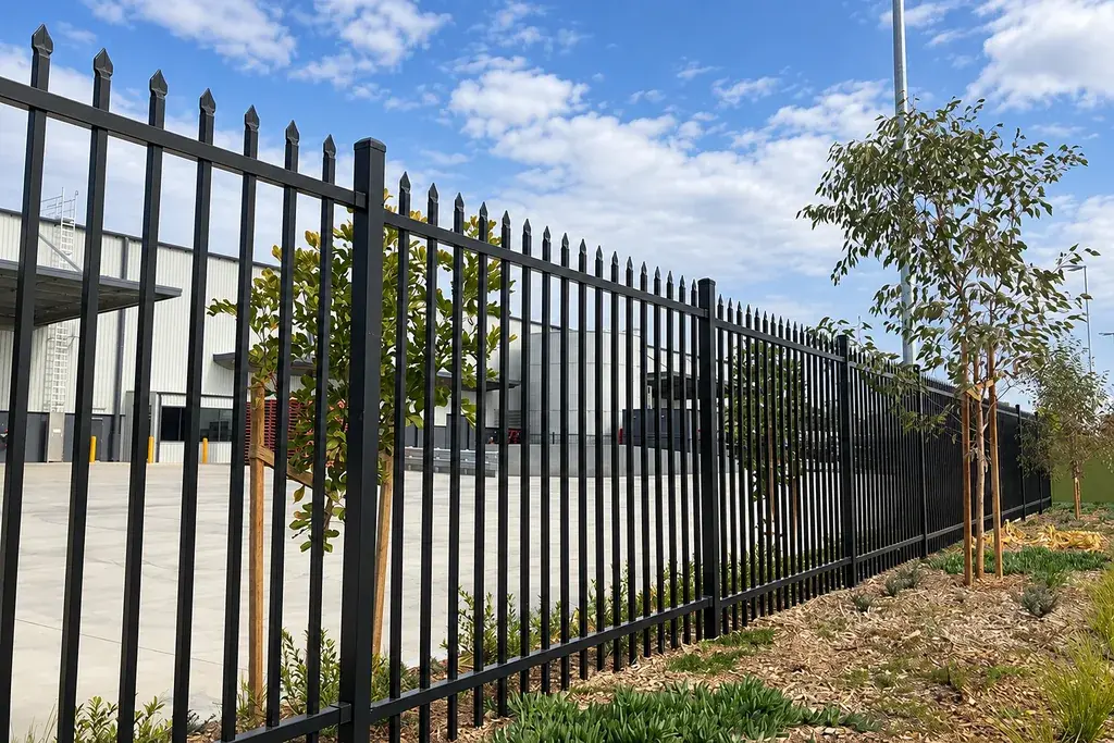 Black steel perimeter fence alongside a warehouse building