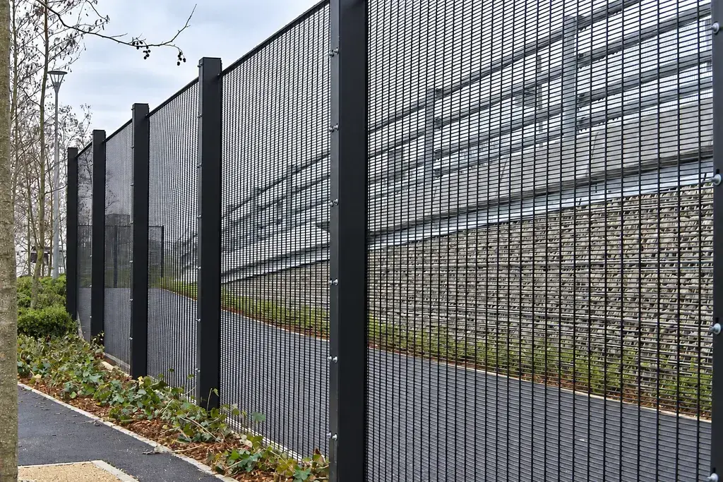 Close mesh metal perimeter fence beside a paved path
