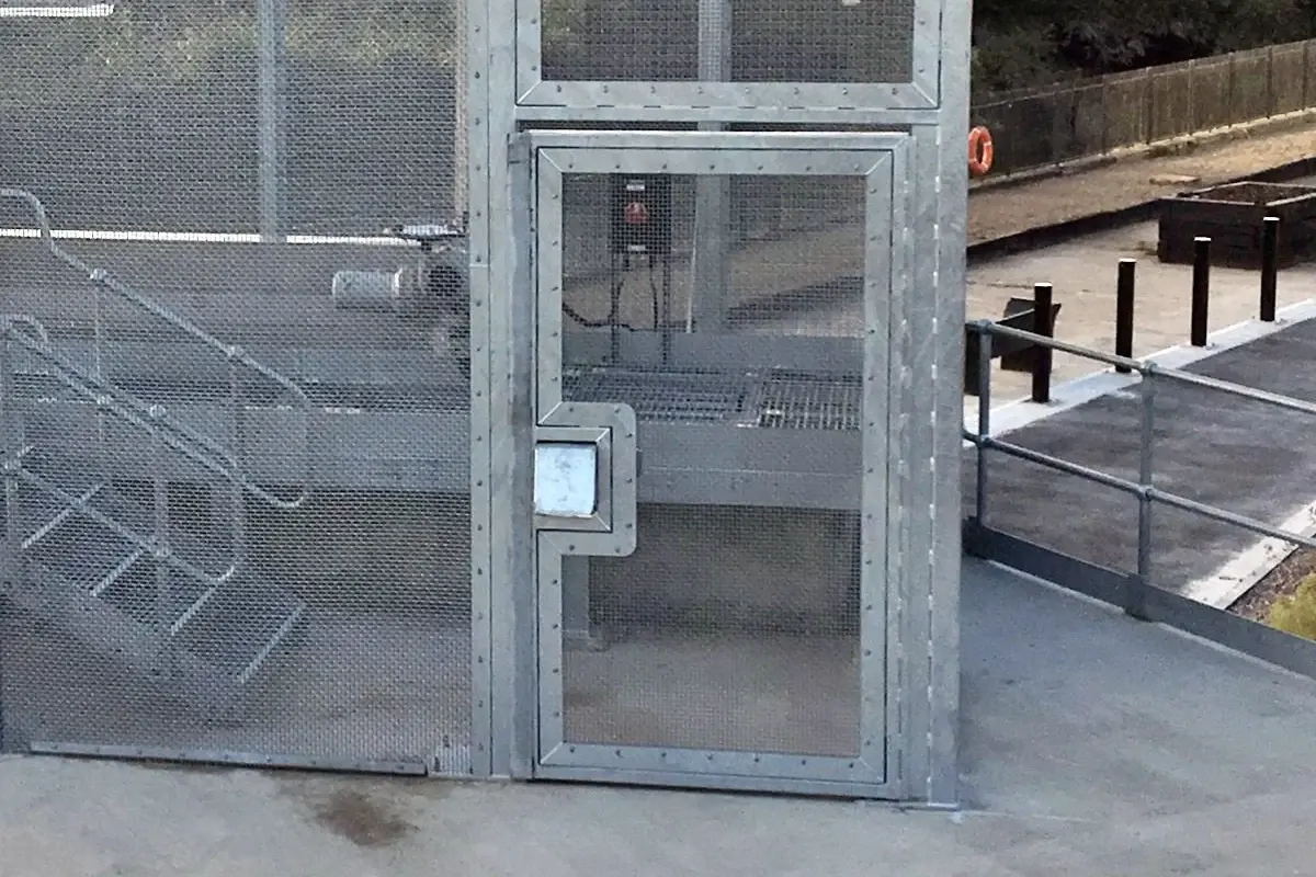 Metal mesh pedestrian gate with frame, latch and adjacent fence