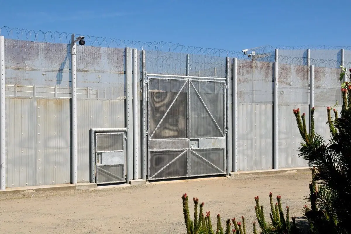 Metal mesh gate in a high perimeter fence with security topping