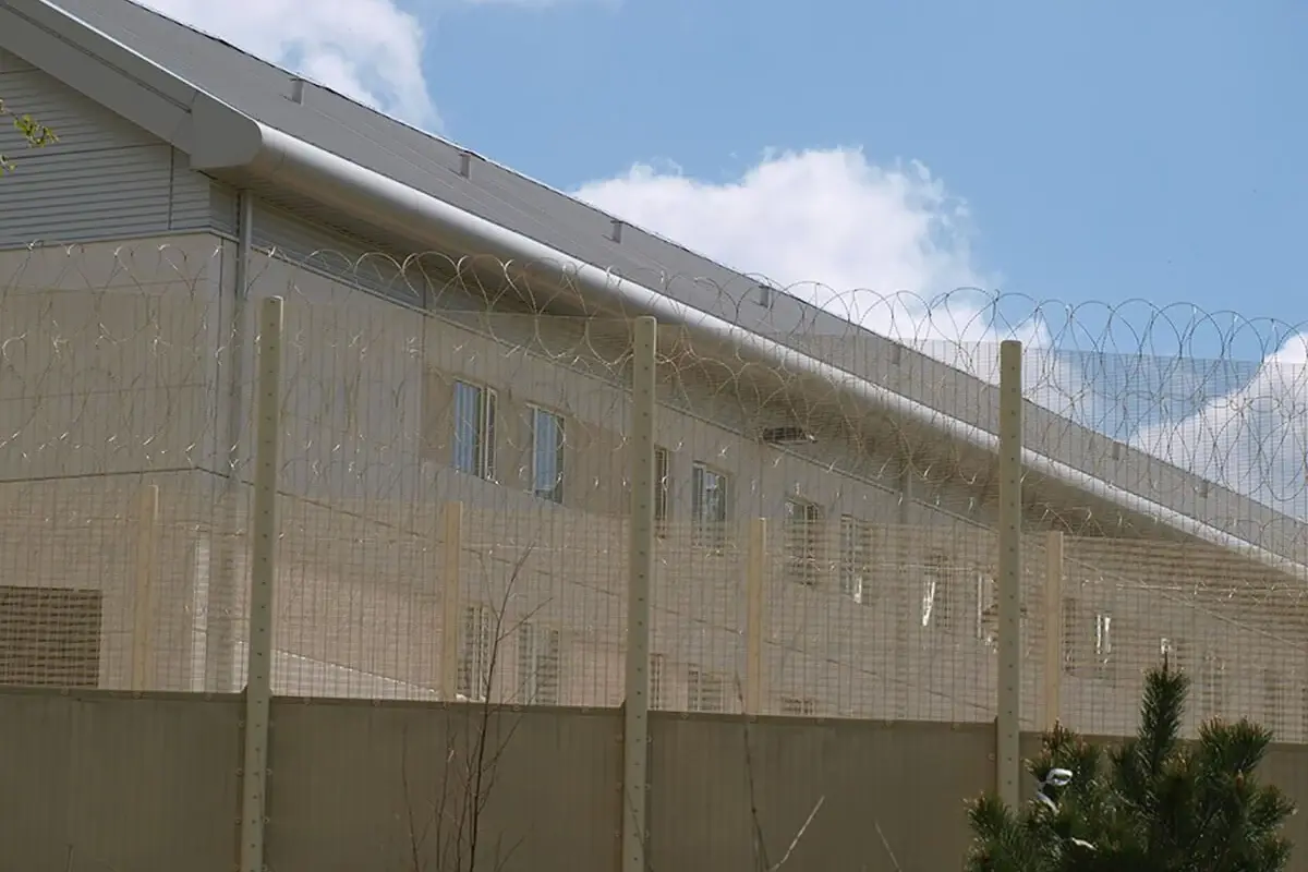 Tall metal mesh perimeter fence beside a custodial building