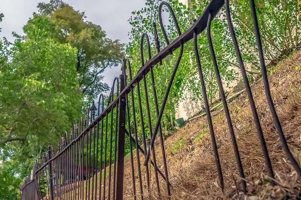 Bent black metal fence panels on sloping ground