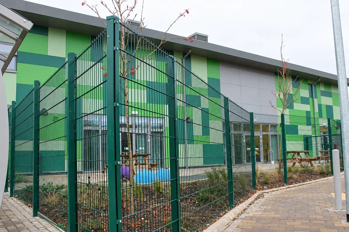 Green welded mesh fence beside paving and a school building