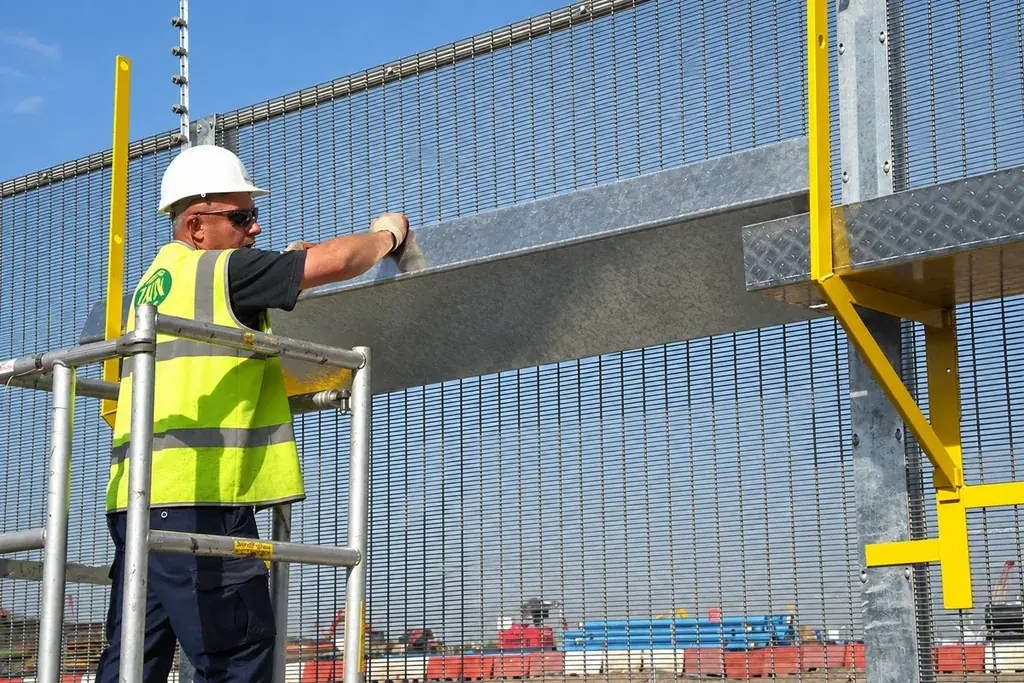 Worker fitting a metal panel to a mesh perimeter fence