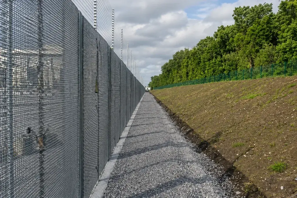 Close mesh perimeter fence running beside a gravel access path