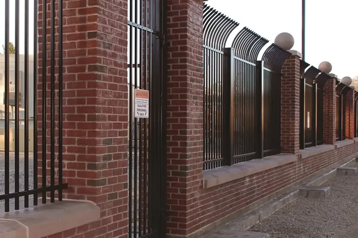 Black steel fence between brick pillars along a paved frontage