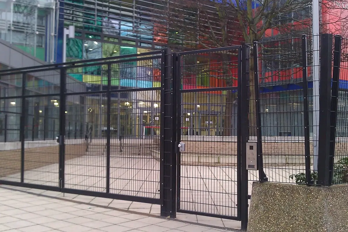 Black mesh swing gate with adjacent fence panels and posts at a building entrance
