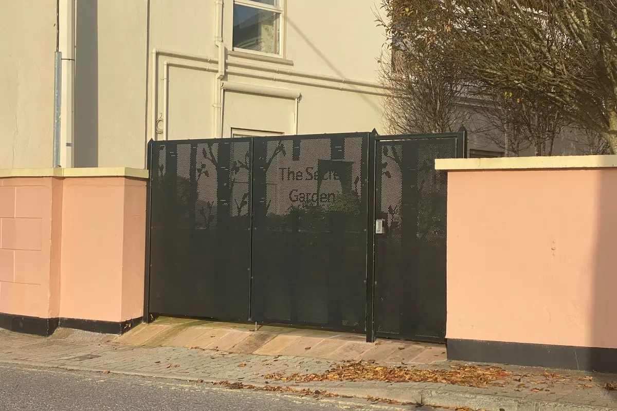 Dark perforated metal garden gate between low boundary walls