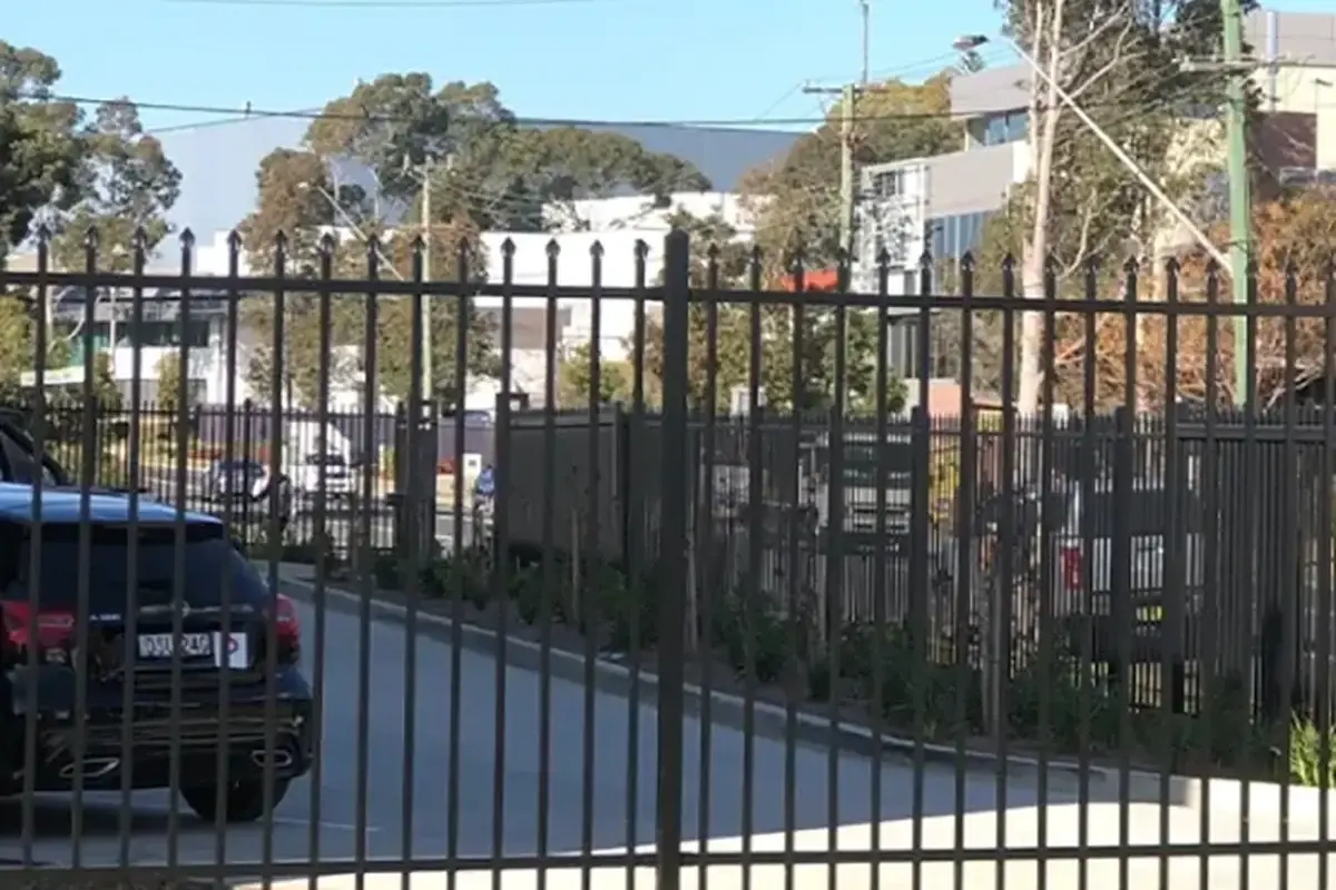 Black steel perimeter fence beside a parking area with cars behind it