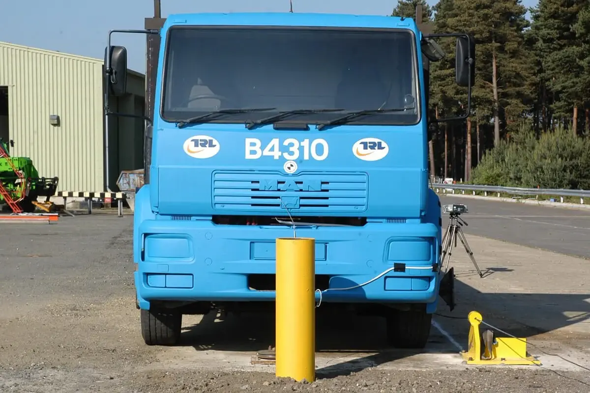 Yellow steel bollard in front of a blue truck at a vehicle test site