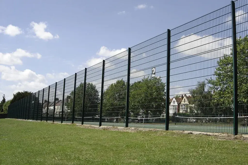 Tall green welded mesh fence running alongside an outdoor sports court