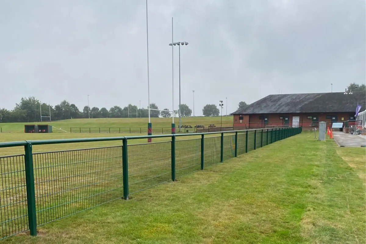 Green spectator rail separating a grass sports field from an outer route