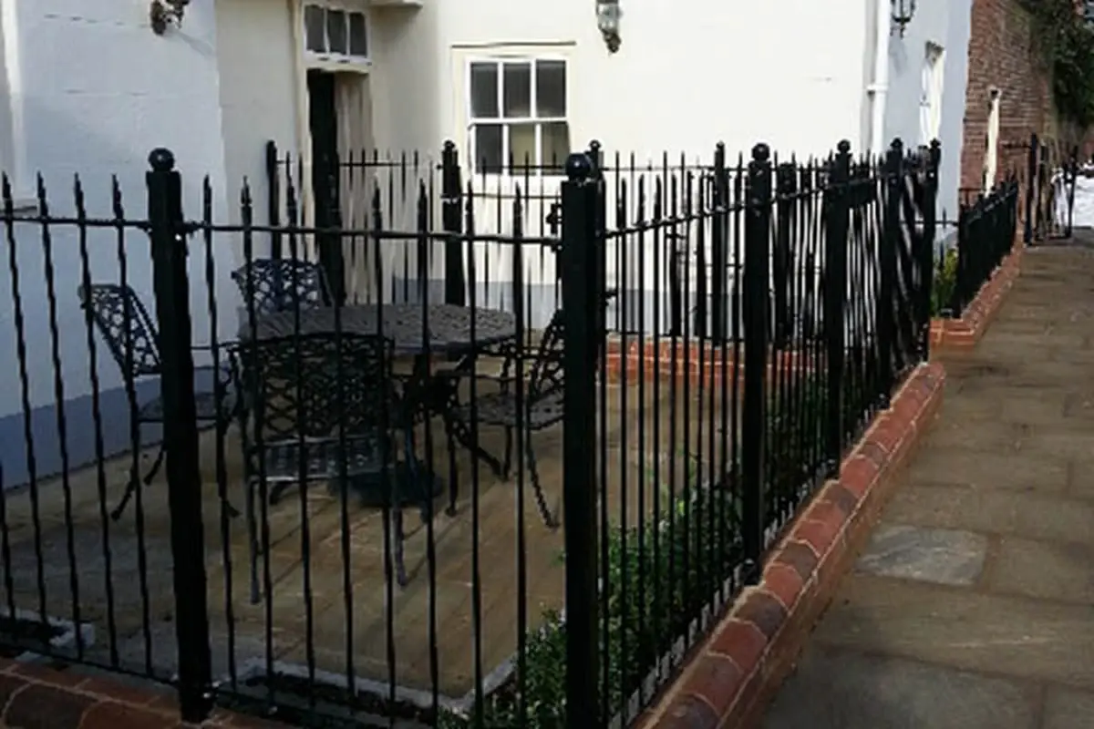 Black metal railings fixed along a low brick wall outside a white building