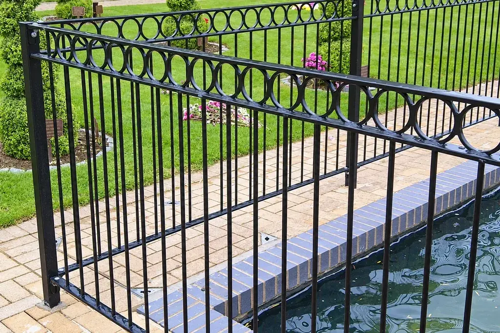 Black railing with circular ornament above vertical bars beside a paved path