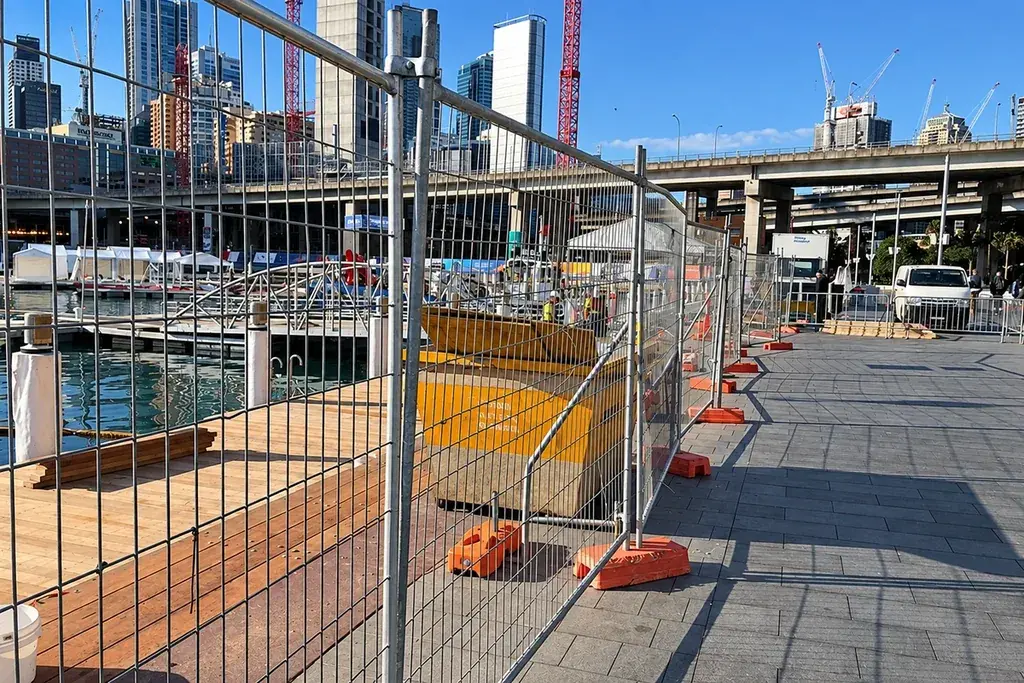Temporary welded mesh fence with braced panels beside a paved public walkway