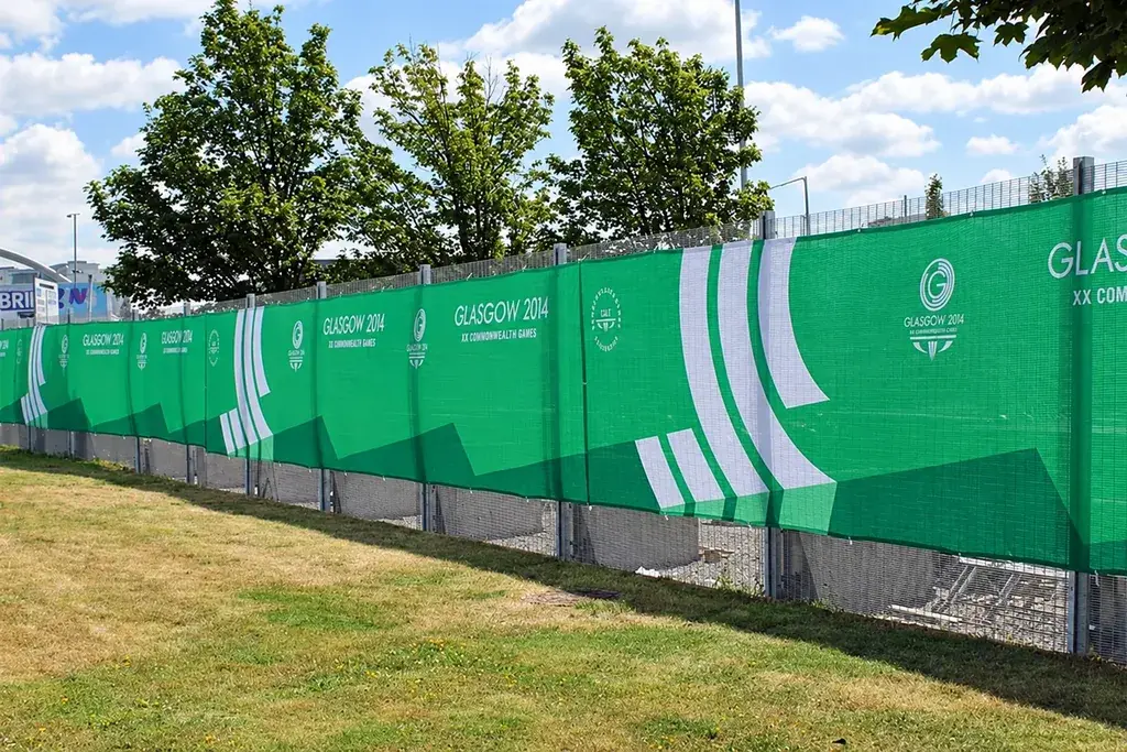 Temporary fence covered with green event screening beside a grass area