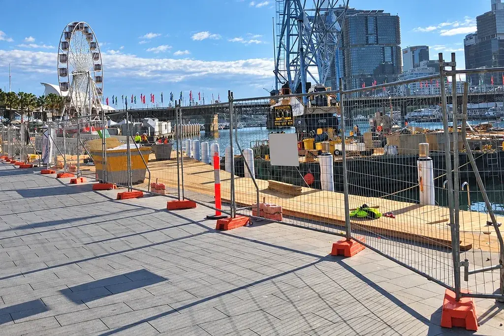 Temporary fence line beside active construction equipment and a pedestrian route